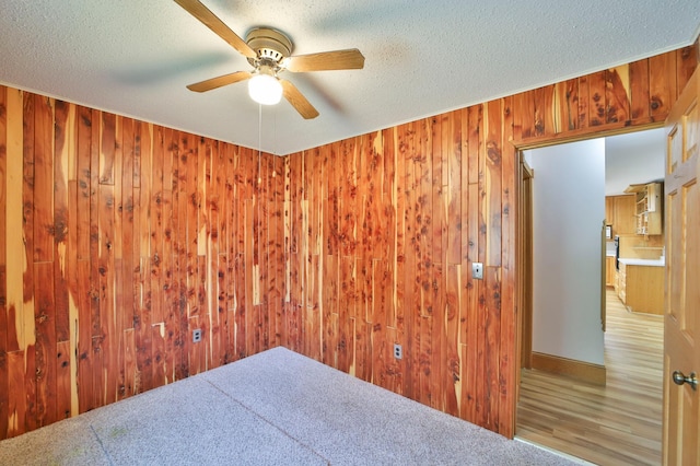 spare room featuring ceiling fan, a textured ceiling, and wood walls