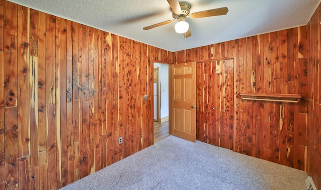 unfurnished room featuring carpet flooring, a textured ceiling, a ceiling fan, and wooden walls