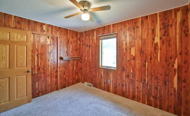 unfurnished room with a ceiling fan, visible vents, carpet floors, wood walls, and a textured ceiling