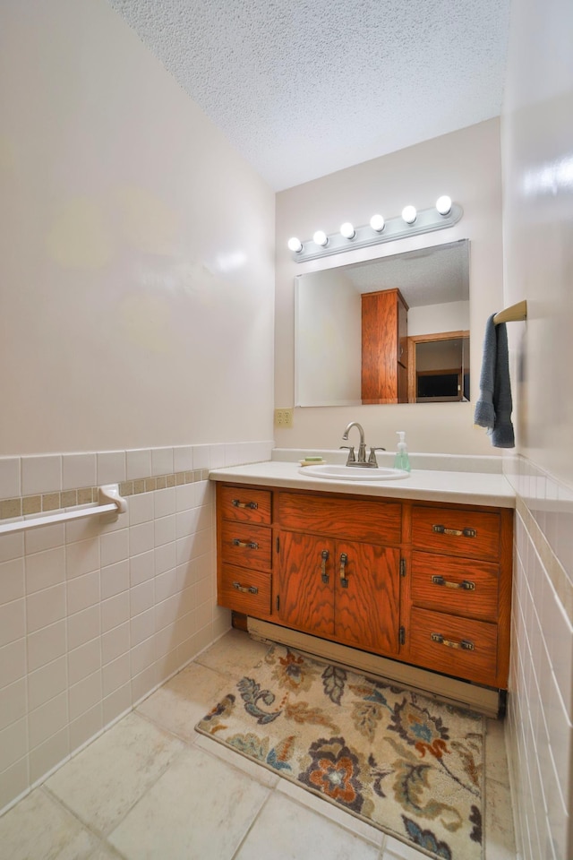 bathroom featuring vanity, tile walls, wainscoting, and a textured ceiling