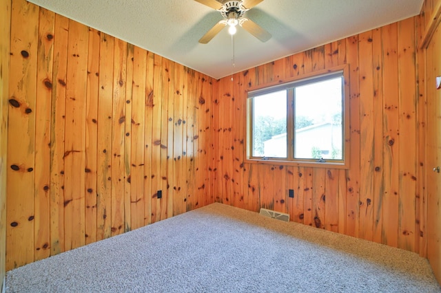 empty room featuring a ceiling fan, visible vents, wood walls, and a textured ceiling