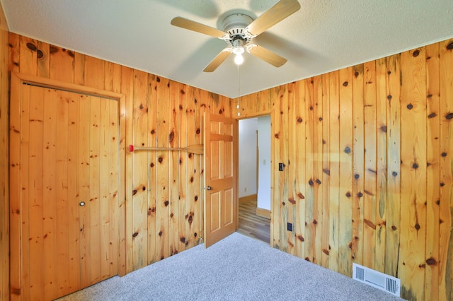 carpeted empty room with visible vents, wood walls, a textured ceiling, and a ceiling fan