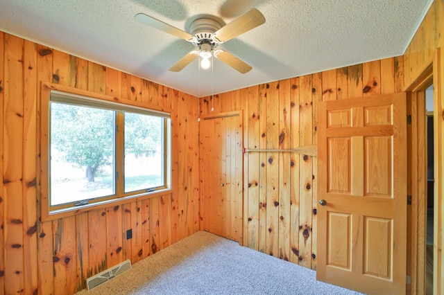 empty room featuring visible vents, wooden walls, ceiling fan, carpet flooring, and a textured ceiling