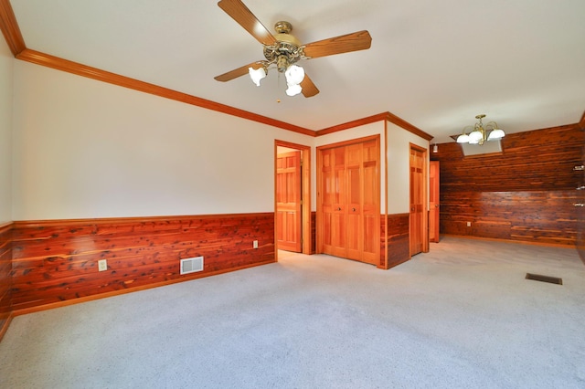 empty room featuring wooden walls, a wainscoted wall, visible vents, ornamental molding, and light colored carpet