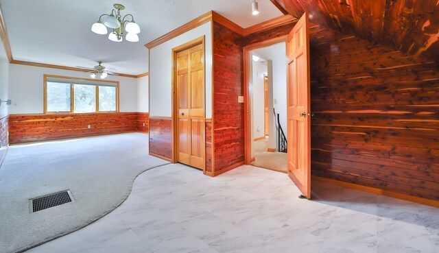 carpeted spare room with wooden walls, visible vents, a wainscoted wall, ornamental molding, and marble finish floor