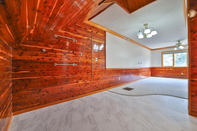 unfurnished room featuring wooden walls, lofted ceiling, wainscoting, a textured ceiling, and crown molding