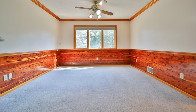 empty room featuring wooden walls, visible vents, a wainscoted wall, ornamental molding, and carpet flooring