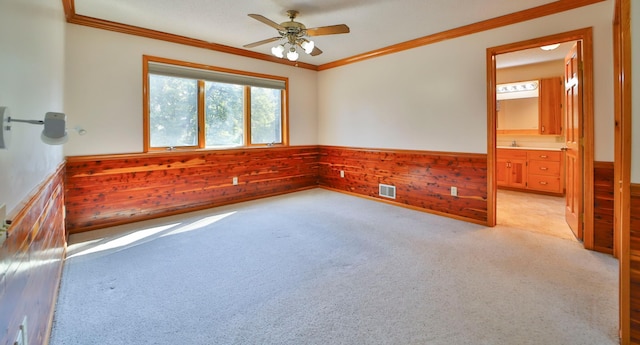 empty room with a wainscoted wall, wood walls, light colored carpet, and ornamental molding