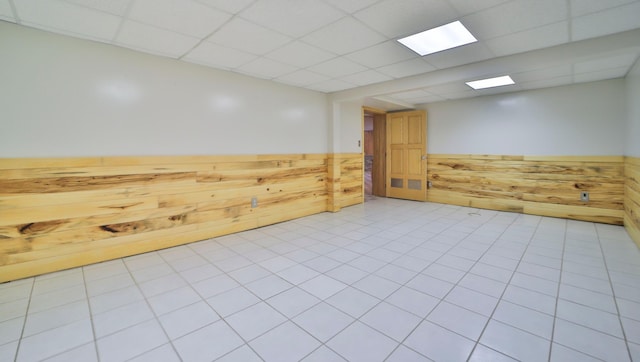 unfurnished room featuring wooden walls, a drop ceiling, and wainscoting