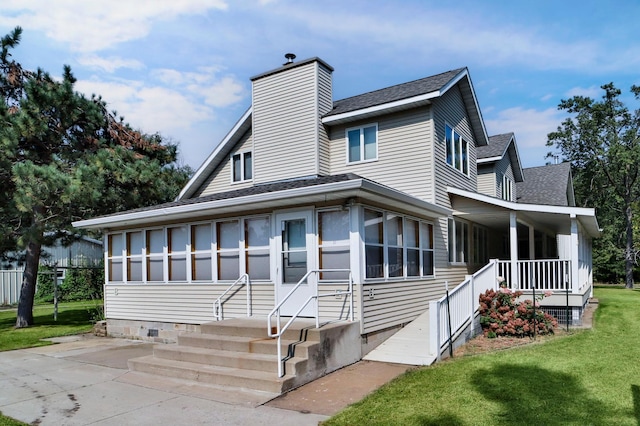 view of front of home featuring roof with shingles, a front yard, covered porch, a chimney, and a sunroom