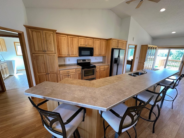 kitchen featuring a kitchen bar, high vaulted ceiling, appliances with stainless steel finishes, and light hardwood / wood-style floors