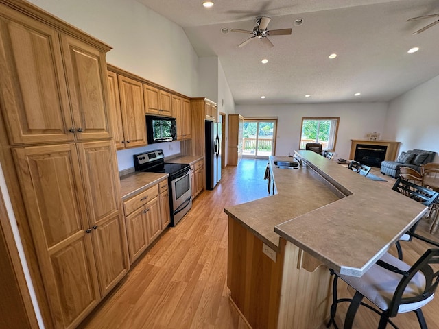 kitchen with stainless steel appliances, light hardwood / wood-style floors, a breakfast bar area, ceiling fan, and lofted ceiling