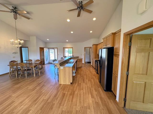 kitchen featuring decorative light fixtures, stainless steel refrigerator, sink, light hardwood / wood-style floors, and a kitchen breakfast bar