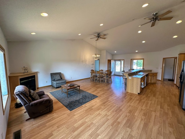 living room featuring ceiling fan with notable chandelier, light hardwood / wood-style flooring, sink, and vaulted ceiling