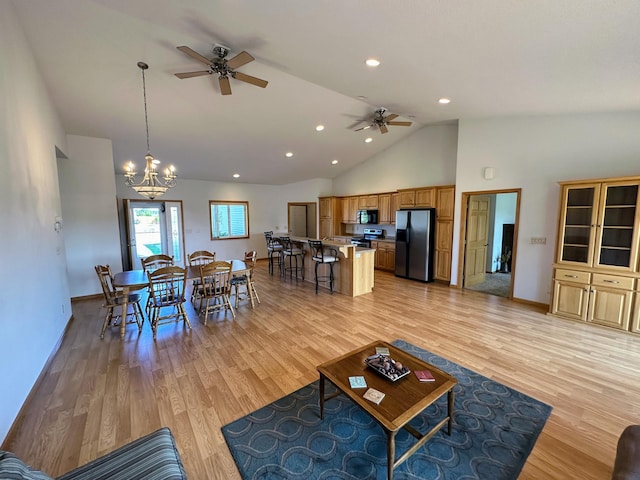 living room featuring ceiling fan with notable chandelier, light hardwood / wood-style floors, and high vaulted ceiling