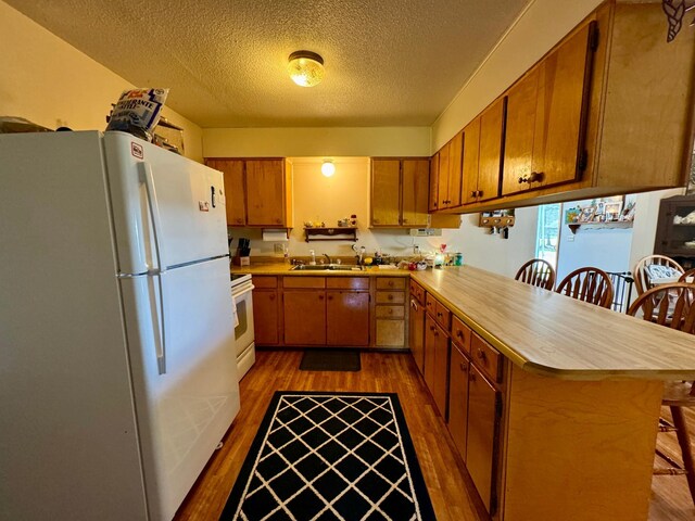 kitchen with dark wood-type flooring, a breakfast bar area, white appliances, and kitchen peninsula