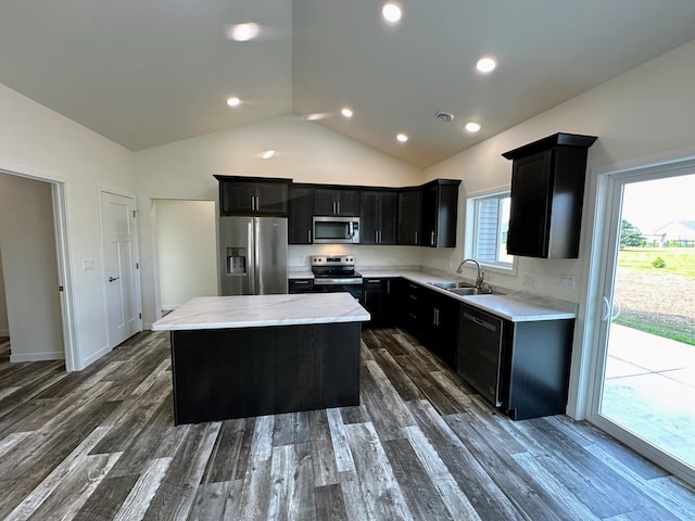 kitchen featuring appliances with stainless steel finishes, a center island, dark cabinetry, lofted ceiling, and a sink
