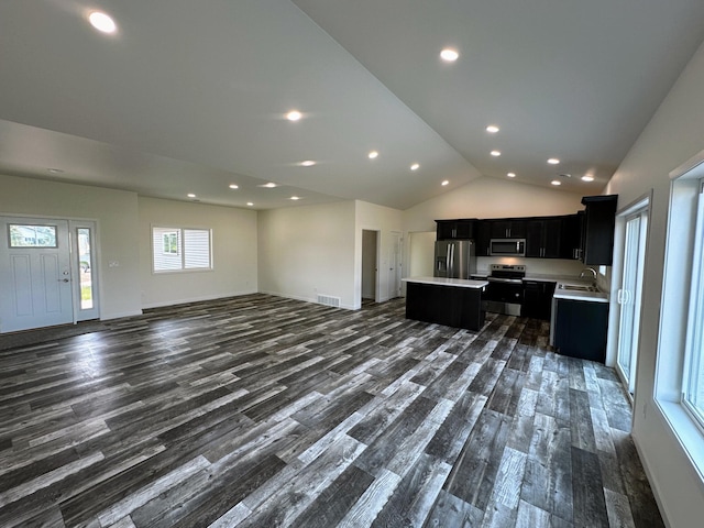 kitchen with open floor plan, light countertops, an island with sink, dark cabinets, and stainless steel appliances