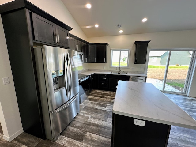 kitchen with light stone counters, lofted ceiling, a kitchen island, dark wood-type flooring, and stainless steel appliances