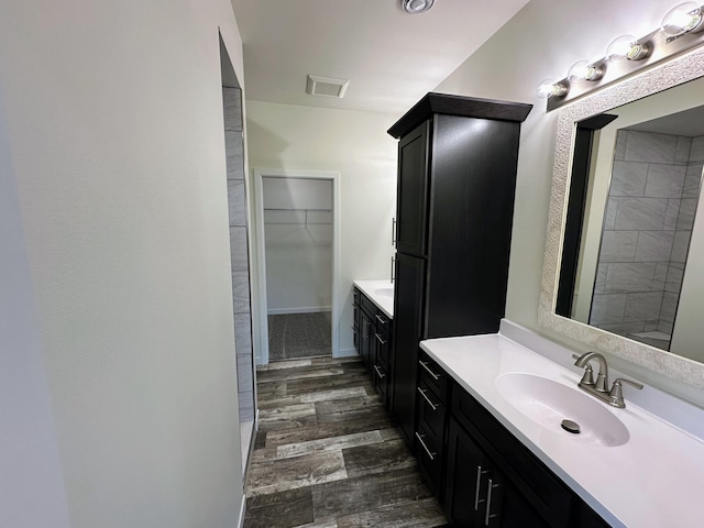 full bath featuring two vanities, a spacious closet, visible vents, wood finished floors, and a sink
