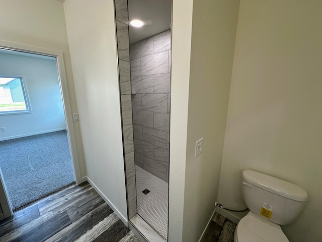 bathroom with a tile shower, wood finished floors, baseboards, and toilet