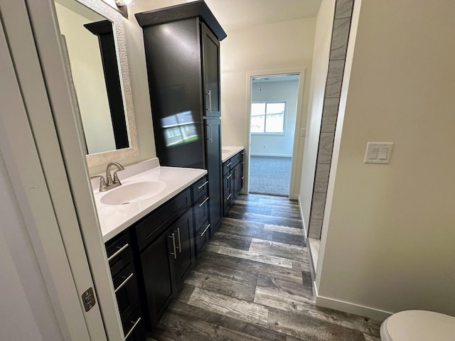 bathroom with toilet, vanity, wood finished floors, and baseboards