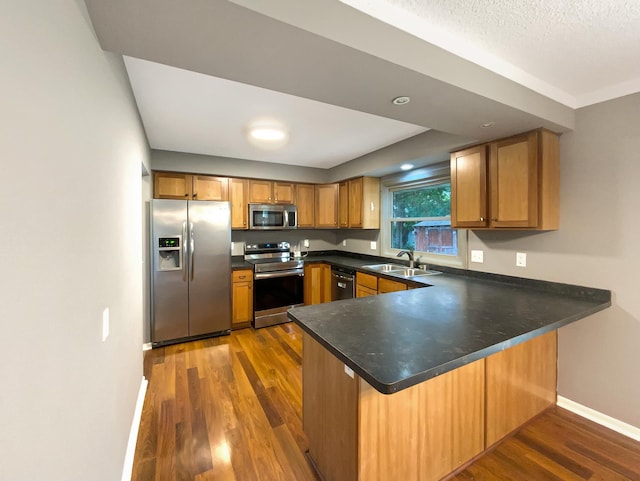 kitchen with sink, kitchen peninsula, a textured ceiling, dark wood-type flooring, and stainless steel appliances