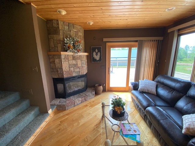 living room featuring wood ceiling, a stone fireplace, and wood-type flooring