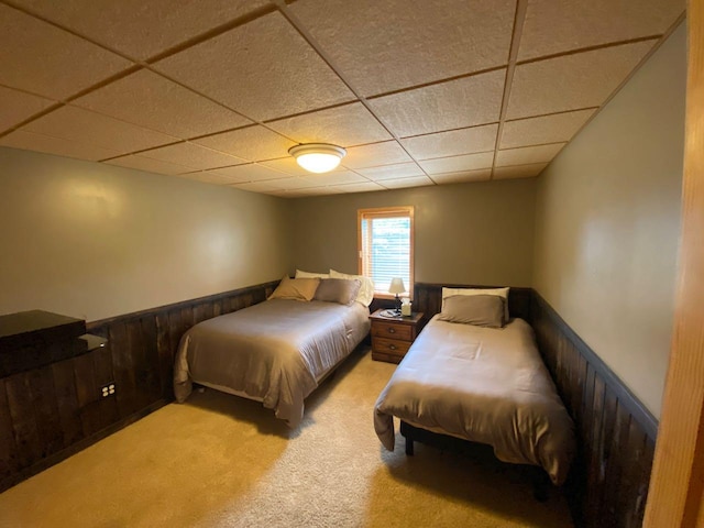 bedroom with wooden walls, a paneled ceiling, and light colored carpet