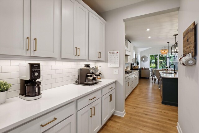 kitchen with tasteful backsplash, white cabinetry, sink, and light hardwood / wood-style flooring