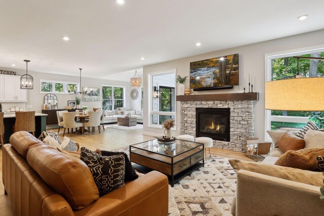 living room with a fireplace, an inviting chandelier, light hardwood / wood-style flooring, and a healthy amount of sunlight