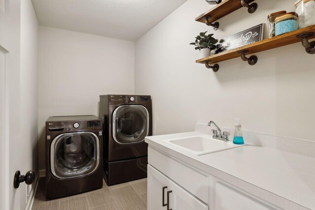 washroom featuring a textured ceiling, washer and clothes dryer, sink, and cabinets