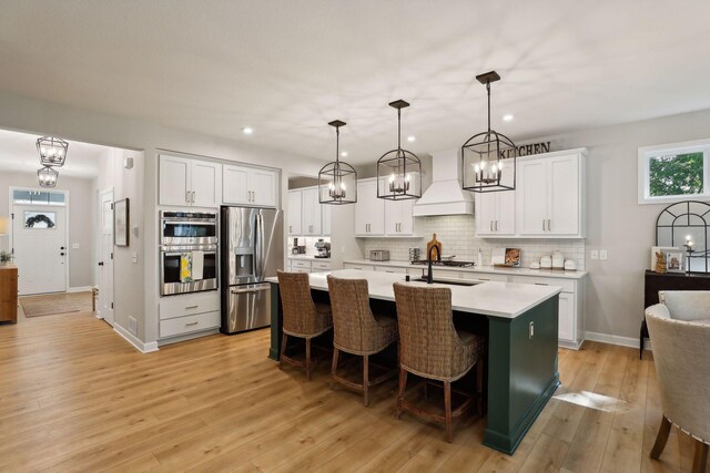 kitchen featuring premium range hood, light hardwood / wood-style floors, hanging light fixtures, white cabinetry, and appliances with stainless steel finishes