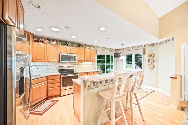 kitchen with a kitchen island, light hardwood / wood-style flooring, sink, stainless steel appliances, and a kitchen bar