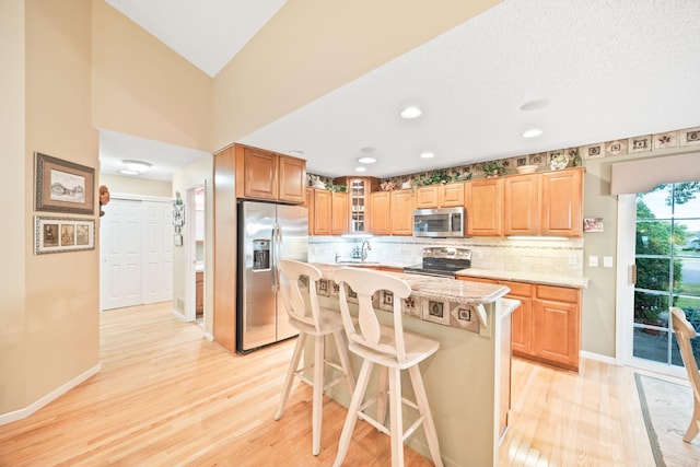 kitchen with stainless steel appliances, backsplash, light wood-style flooring, a sink, and a kitchen bar