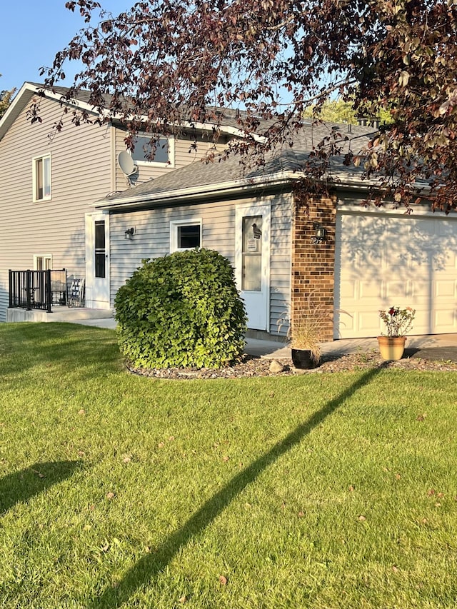 rear view of property with a lawn, an attached garage, and a shingled roof