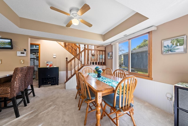 dining area with a ceiling fan, a wainscoted wall, light carpet, and stairs