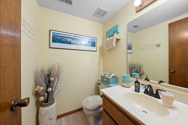 bathroom featuring a textured ceiling, visible vents, toilet, wood finished floors, and vanity