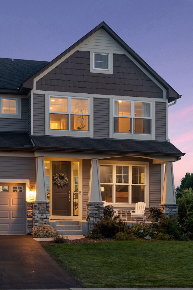 craftsman inspired home with a porch, a lawn, stone siding, and a shingled roof