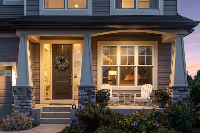 exterior entry at dusk with a porch and a shingled roof