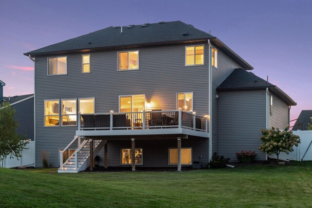 back of house at dusk featuring stairway, a deck, a lawn, and a shingled roof