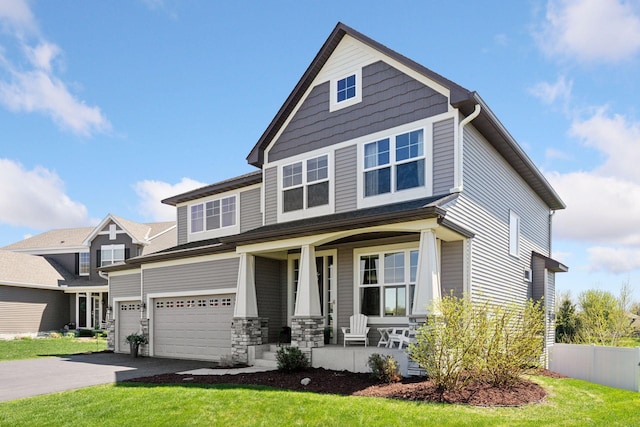 craftsman house featuring covered porch, driveway, an attached garage, and stone siding