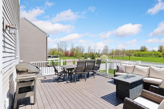 deck with outdoor dining space, an outdoor living space with a fire pit, a lawn, grilling area, and view of wooded area