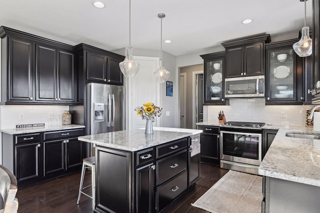kitchen with stainless steel appliances, dark cabinetry, a sink, backsplash, and glass insert cabinets