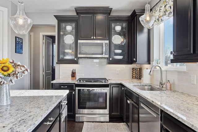 kitchen featuring stainless steel appliances, a sink, backsplash, light stone countertops, and decorative light fixtures