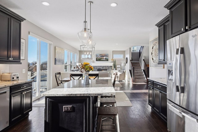 kitchen with stainless steel refrigerator with ice dispenser, a kitchen bar, dark wood-type flooring, dark cabinetry, and a stone fireplace