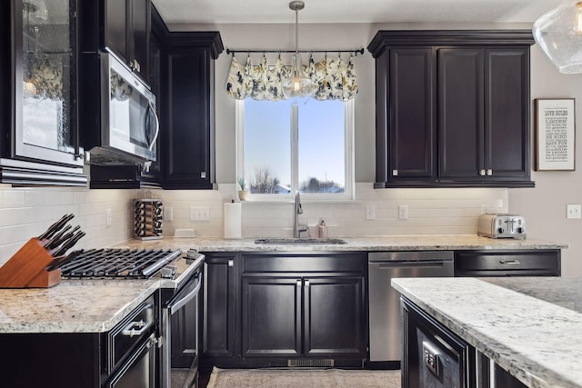 kitchen with a sink, appliances with stainless steel finishes, tasteful backsplash, dark cabinets, and light stone counters