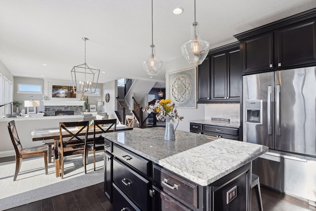 kitchen with stainless steel refrigerator with ice dispenser, dark wood-style flooring, a stone fireplace, open floor plan, and recessed lighting