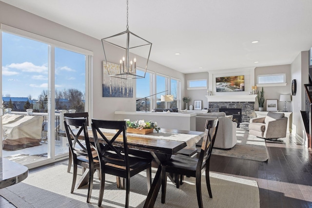 dining room featuring a stone fireplace, a chandelier, healthy amount of natural light, hardwood / wood-style flooring, and recessed lighting