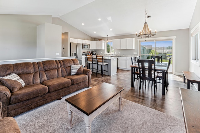 living room with wood-type flooring, a wealth of natural light, a notable chandelier, and vaulted ceiling